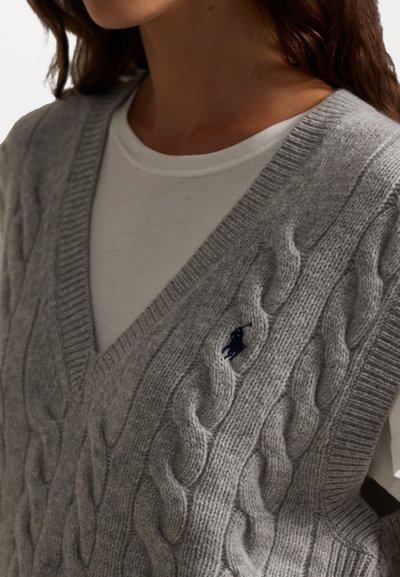 Vesta gri din tricot cu model în relief, având un decolteu în V și margini zimțate, adorned cu un mic logo bleumarin pe față.