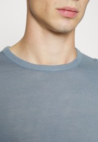 Light blue knitted sweater with a round neckline. The texture is fine ribbed, showing smooth and stretchy fabric without visible patterns.