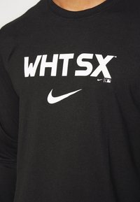 Czarna, długorękawowa koszulka z wyraźnym białym napisem "WHTSX" oraz małym logo Nike w kształcie łyżwy. Materiał wydaje się być miękki o gładkiej fakturze.