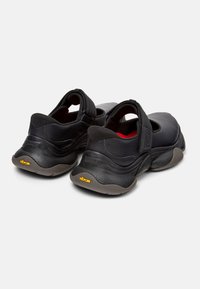 Scarpe nere con finitura testurizzata, fascia in Velcro e suola in gomma spessa con logo giallo Vibram. Progettate per comfort e stabilità.