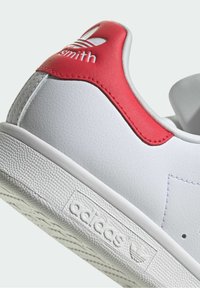 Tallone di una sneaker Adidas bianca con accento rosso e scritta "smith", che mostra la suola testurizzata e il logo sul battistrada.