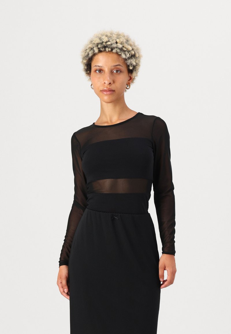 Schwarzes Kleid mit einem transparenten langärmeligen Oberteil und einem soliden Rock mit elastischem Taillenbund. Glatte Textur, taillierte Passform und minimalistischer Stil.