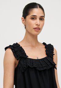 Top nero senza maniche con scollatura arricciata e spalline. Realizzato in tessuto morbido, ha una vestibilità morbida e una superficie liscia.