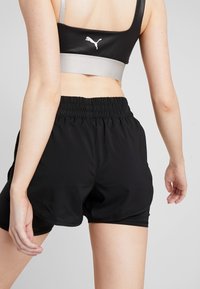 Pantalones cortos deportivos negros con cintura elástica, combinados con un sujetador deportivo negro y plateado que presenta un logo en la parte posterior. Textura de tela suave.