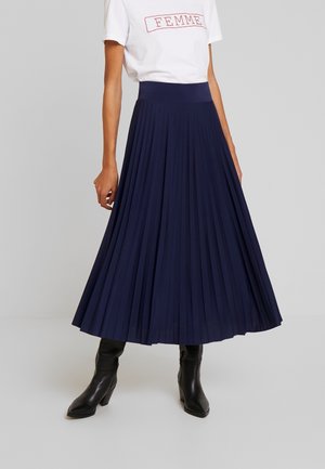 Gonna midi plissettata blu navy con vita alta, realizzata in tessuto leggero, abbinata a una T-shirt bianca con scritte rosse.