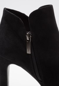 Schwarzer Wildleder-Stiefelette mit einem hohen Stiletto-Absatz. Verfügt über einen seitlichen Reißverschluss für den Verschluss und eine glatte Textur im oberen Bereich.