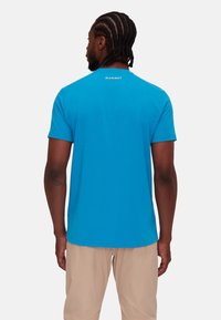 Blå kortärmad t-shirt i bomull med rundad halsringning och en logotyp tryckt på övre ryggen. Texturerad tygfinish.