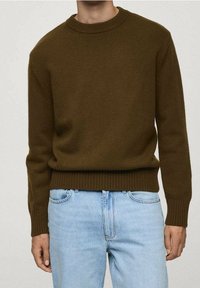 Brauner gestrickter Pullover mit geripptem Rundhalsausschnitt und Saum, kombiniert mit hellblauen Jeans, die die Textur und die taillierte Passform betonen.