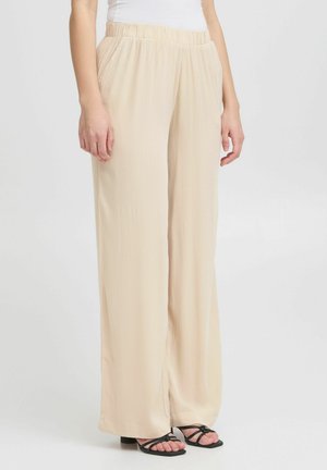 Beige weite Hosen aus leichtem Stoff mit elastischem Bund und Seitentaschen, kombiniert mit schwarzen Sandalen mit Riemen.