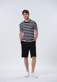 Stribet sort og hvid kortærmet t-shirt parret med sorte shorts og hvide sneakers, med en afslappet pasform og glat stoftekstur.
