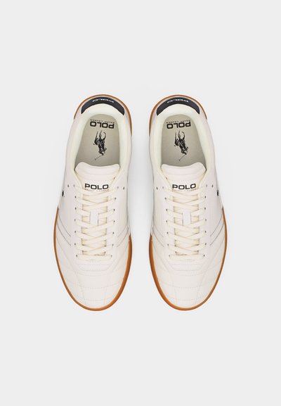 Ζευγάρι λευκά αθλητικά παπούτσια Polo Ralph Lauren με σόλες από καουτσούκ και μαύρο λογότυπο αναβάτη πόλο εμφανές μέσα σε κάθε παπούτσι.