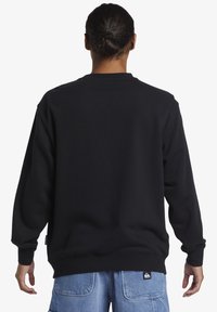 Schwarzes Sweatshirt mit langen Ärmeln, gerippten Bündchen und Saum, entworfen mit einem lockeren Schnitt. Der Stoff wirkt glatt und weich.