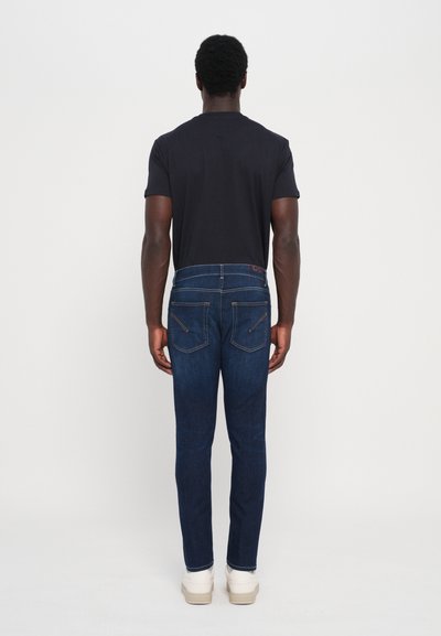 Jeans din denim de un albastru închis, cu o croială slim, având o talie medie, cusături contrastante subtil și două buzunare la spate.