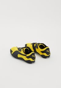 Yellow and black athletic shoes with a textured upper, a rounded shape, and rubber outsole featuring spikes for traction.