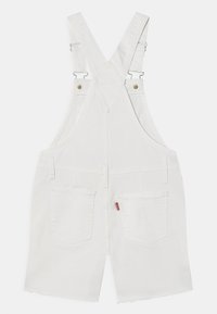 Λευκά τζιν καμπριόν με ρυθμιζόμενες τιράντες, που διαθέτουν δύο πίσω τσέπες και φθαρμένο τελείωμα. Χρυσές μεταλλικές λεπτομέρειες.