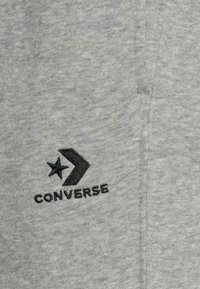Tessuto di cotone grigio con un logo "Converse" ricamato in nero, caratterizzato da un design a stella e freccia. La texture è liscia e leggermente melangiata.