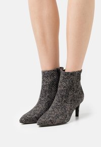 Stivaletti con punta affusolata, caratterizzati da un motivo a spina di pesce in nero e beige. Realizzati in materiale testurizzato con un tacco sottile.