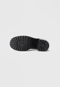 Semelle en caoutchouc noir avec un motif de grip texturé, forme arrondie et bords contrastés. Présente des détails en relief et une surface lisse.