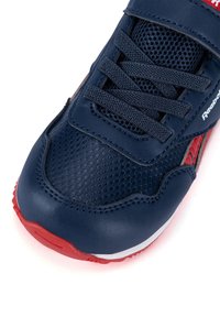 Zapatilla deportiva azul que presenta una mezcla de texturas de cuero suave y malla, con acentos rojos y un sistema de lazadas y tiras de velcro aseguradas.