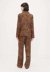 Pajama set z leopardskim vzorcem v rjavi in črni barvi, z dolgimi rokavi, sproščenim krojem in vzorčenimi manšetami. Mehka tkanina z gladko teksturo.