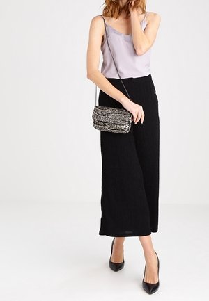 Sorte bredbenede bukser lavet af tekstureret stof, parret med en lys lilla camisole og en glitrende, sølvfarvet crossbody taske. Sorte pumps fuldender looket.