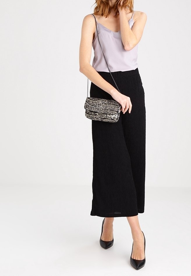 Pantaloni neri a gamba larga in tessuto testurizzato, abbinati a un top in raso viola chiaro e a una borsa a tracolla scintillante argentata. Scarpe col tacco nere completano l'outfit.