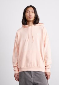 Ροζ φούτερ από απαλό ύφασμα με τσέπη καγκουρό και ρυθμιζόμενα κορδόνια. Διαθέτει ένα μικρό λευκό λογότυπο Nike στο στήθος.