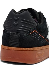 Svart mocka och gummiskor med en texturerad svart häl, orange detaljer och en gummisula med ett varumärkesdetalj.