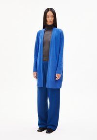 Lange open voorkant cardigan in felblauw, gecombineerd met een grijze top en bijpassende blauwe wijde broek. Glad textuur met ribgebreide accenten.