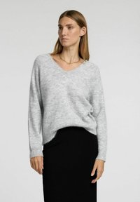 Grå strikket sweater med V-hals, lange ærmer og en afslappet pasform, parret med en sort nederdel. Blød tekstur og slightly længere bagkant.