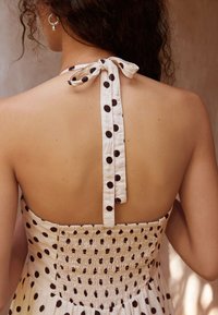 Kleidi tagumine osa, kus on paela kinnitusega kaelus, kreemikas kangas mustade täppidega ja smock-detailidega seljaosas.