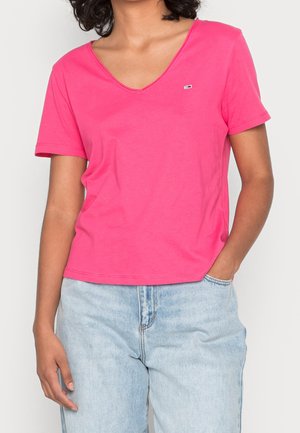 Roze T-shirt met korte mouwen en een V-hals, met een klein logo op de linkerkant van de borst, gemaakt van een zachte katoenmix. Gecombineerd met lichtblauwe spijkerbroek.
