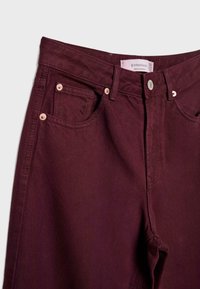 Vinrøde denimjeans med høj talje, udstyret med to forlommer, kobbernitter og en label ved linningen. Glat tekstur.