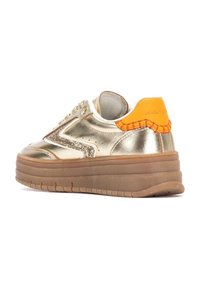 Zapatillas metálicas doradas con acentos brillantes, pestaña de talón naranja y una suela gruesa y texturizada marrón. Presenta costuras decorativas y cierres de cordones.