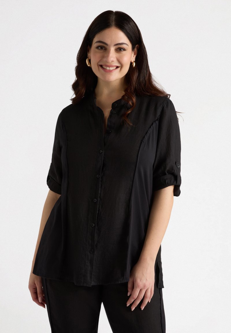 Camisa negra de botones con cuello, mangas cortas enrolladas y aberturas laterales. Fabricada en una tela ligera y suave. Detalles mínimos.