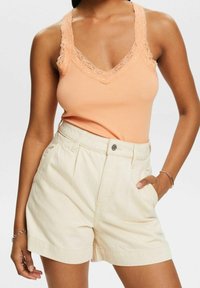 Top de tirantes de melocotón con ribete acanalado y escote de encaje, combinado con pantalones cortos de cintura alta en color crema que cuentan con un botón frontal y bolsillos laterales.