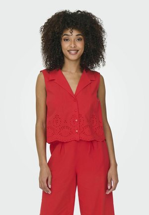 Blusa sin mangas de color rojo con cuello, que presenta detalles de ojetes decorativos y un dobladillo en ondas. Los botones en la parte frontal añaden un toque final.