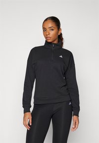 Melnā sudraba krāsa ar rāvējslēdzēju, kas izgatavota no mīkstas auduma. Tai ir augsts apkakle, brīvs piegriezums un Adidas logo baltā krāsā uz krūšu un kreisā piedurknes.