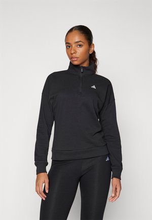 Svart hettejakke med glidelås laget av myk stoff. Har høy krage, avslappet passform, og Adidas-logoen i hvitt på brystet og venstre erme.