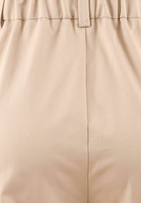 Beige stof met een gladde textuur, met een gegatherde tailleband en verticale naaddetails, ontworpen voor comfort en een ontspannen pasvorm.