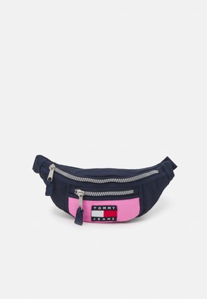 Banane en tissu bleu marine avec un panneau avant rose et une fermeture éclair argentée, arborant un patch logo rectangulaire avec le texte "TOMMY JEANS".
