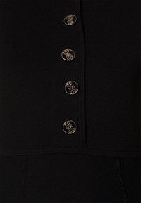 Vêtement en tricot noir orné de quatre boutons en argent décoratifs avec des motifs intriqués, disposés verticalement sur le devant.