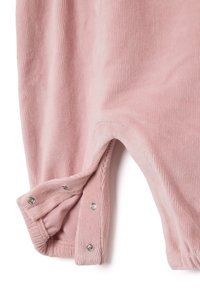 Tessuto di velluto a coste rosa chiaro con bottoni a pressione lungo la cucitura, parte di un polsino o di un'apertura della gamba di un indumento.