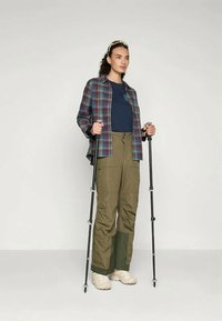 Karirana srajca v modri, zeleni in rdeči barvi, preložena čez mornarsko modro majico; olivno zeleni vojaški hlače in svetle pohodne čevlje; drži pohodne palice.