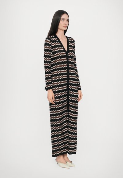 Lange zwarte jurk met een golvend patroon in crème en bruin, met een diepe V-hals, knoopsluiting aan de voorkant en lange mouwen. Glad textuur.