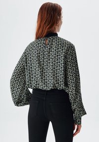 Blusa nera e crema con maniche lunghe e voluminose, chiusura a chiave sul retro e motivo a onde su tessuto testurizzato. Abbinata a jeans neri.