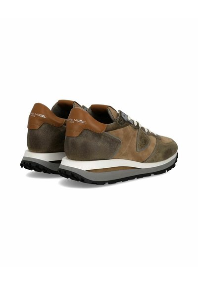 Bruine suède sneakers met een tan leren hieltab, witte tussenzool, zwarte buitenzool en grijze accenten aan de zijkant. Veters in een lichte kleur.