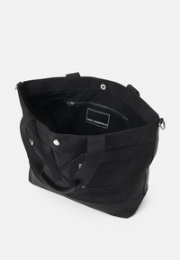 Czarna torba tote z nylonu z podwójnymi uchwytami, wewnętrzną kieszenią na zamek, wytłoczonym logo i zapięciem na zatrzask. Teksturowana dolna część dla zwiększenia trwałości.