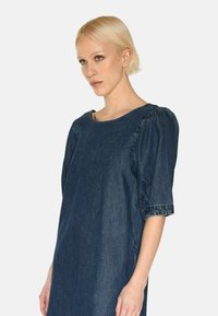 Denimmekko, jossa on pyöreä pääntie, puffatut lyhyet hihat ja väljä istuvuus. Väri on tumma sininen; kankaassa on hieno tekstuuri.