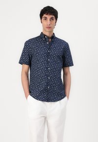 Chemise à manches courtes, boutonnée, en tissu bleu marine avec un motif paisley dans des teintes claires. Dispose d'un col classique et de boutons.